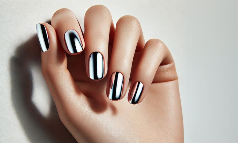 A simple image of a single hand with well-manicured nails painted in a metallic silver chrome polish. The nails have a smooth and reflective finish. The background is plain white, emphasizing the minimalist and elegant design.